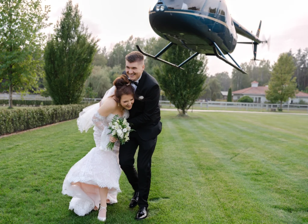 Dynamiczne ujęcie pary młodej na tle startującego helikoptera. Nowoczesna fotografia ślubna Warszawa – spektakularny reportaż ślubny.