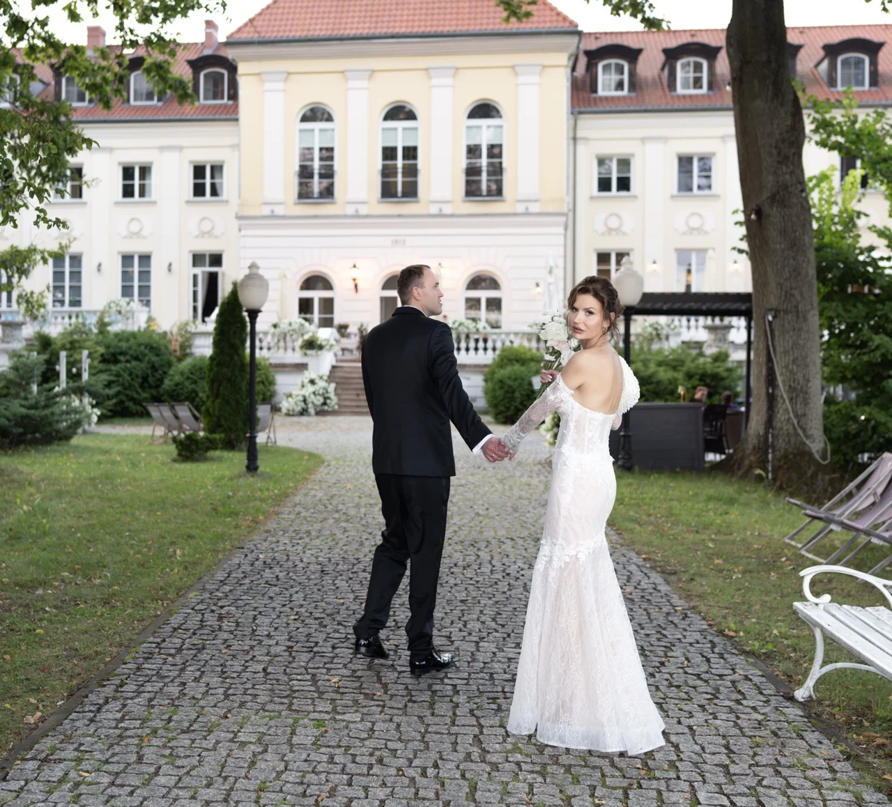 Nowożeńcy idą alejką w ogrodzie Pałacu Alexandrinum