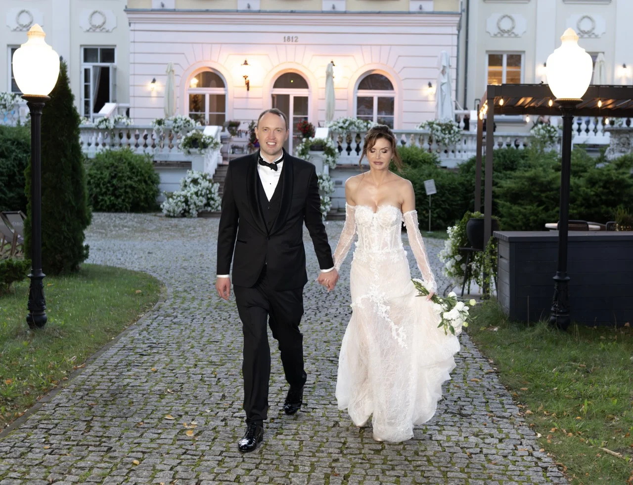 Para młoda idzie aleją w ogrodzie Pałacu Alexandrinum wieczorem